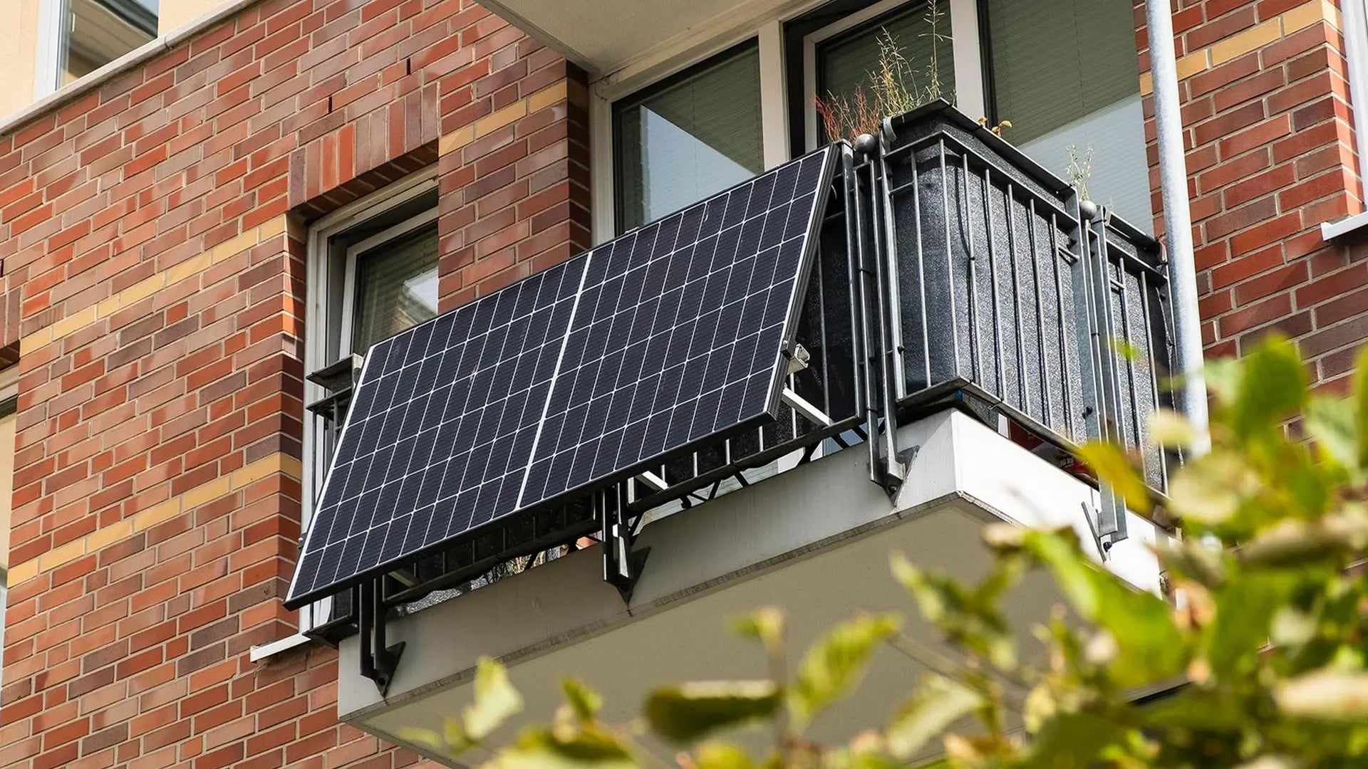 Zwei Solarmodule am Balkongeländer eines Backsteinhauses, an schwarzen Winkeln befestigt