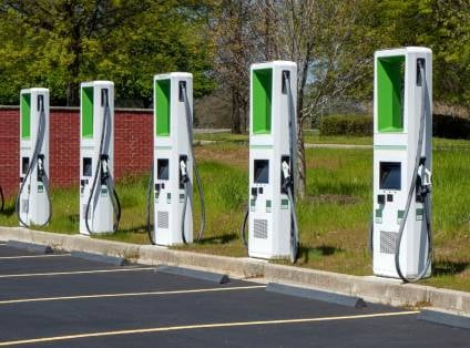 Fünf weiß-grüne Ladesäulen für Elektrofahrzeuge nebeneinander am Rand eines Parkplatzes