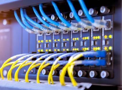 Netzwerkverteiler im Rack mit blauen und gelben Patchkabeln, an den Anschlüssen leuchten gelbe Statusanzeigen