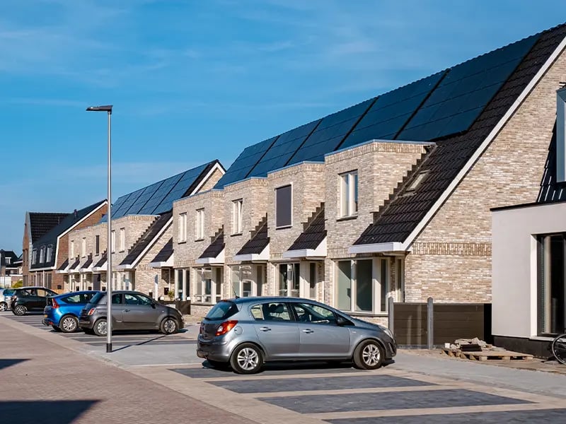 Neubau-Reihenhauszeile aus hellem Klinker, deren Satteldächer durchgehend mit dunklen Solarmodulen belegt sind, davor parkende Autos