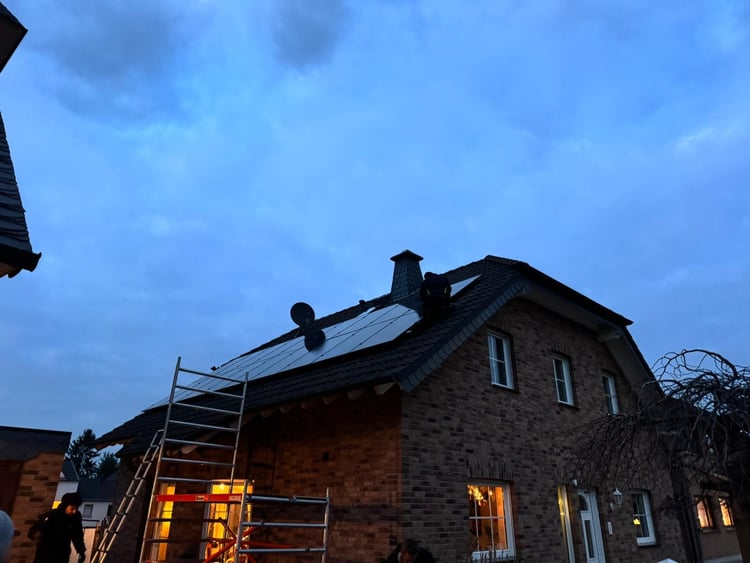 Backsteinhaus in Düren in der Abenddämmerung: Leiter und Gerüst an der Fassade, Solarmodule auf dem Dach, erleuchtete Fenster