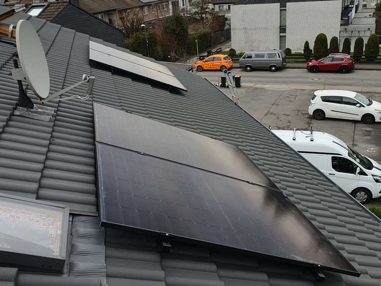 Solarmodule auf einem grauen Ziegeldach in Kornelimünster neben Dachfenster und Satellitenschüssel, darunter eine Wohnstraße mit parkenden Autos