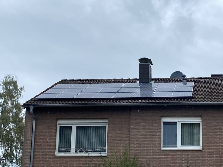 Backsteinhaus in Würselen mit schwarzen Solarmodulen auf dem Ziegeldach, daneben Schornstein und Satellitenschüssel