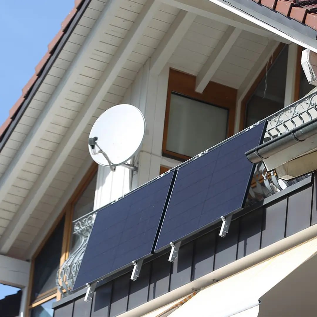 Zwei Solarmodule an der Balkonbrüstung eines Wohnhauses, darüber eine Satellitenschüssel