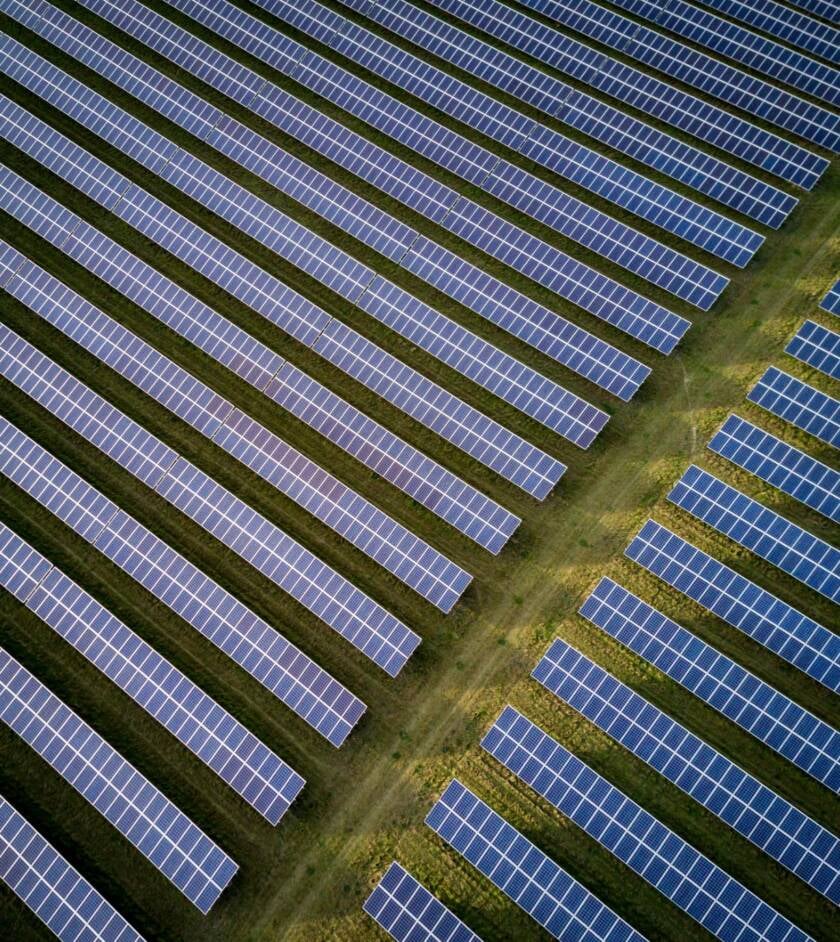 Luftaufnahme einer großflächigen Photovoltaikanlage: lange Modulreihen in gleichmäßigem Abstand