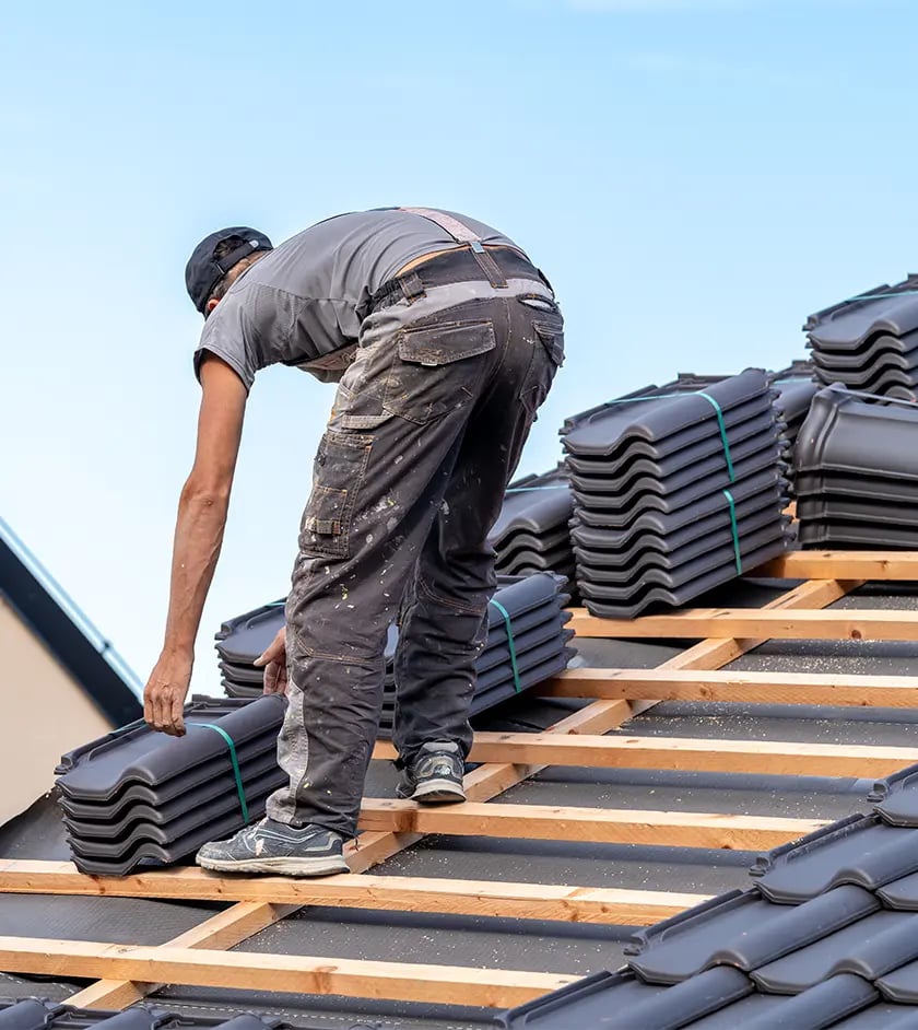 Dachdecker verlegt neue dunkle Dachziegel auf der frisch gedeckten Lattung eines Satteldachs