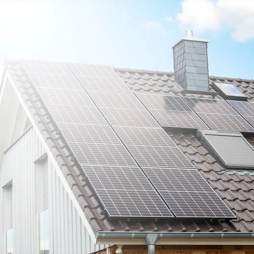 Schwarze Photovoltaikmodule auf dem Ziegeldach eines Wohnhauses, daneben ein verputzter Schornstein