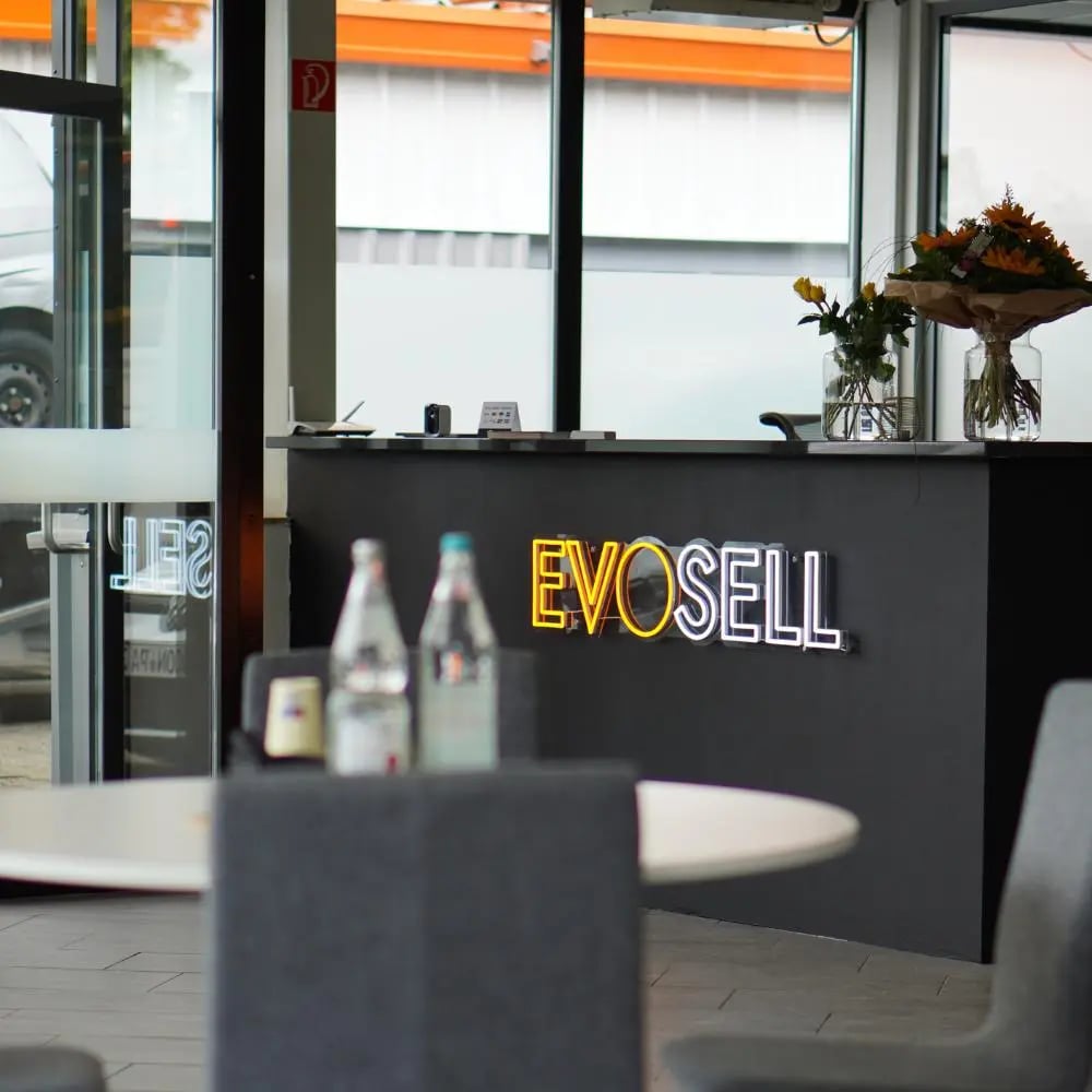 Empfangsbereich des Showrooms: dunkler Tresen mit leuchtendem EvoSell-Schriftzug, davor ein runder Besprechungstisch mit Stühlen