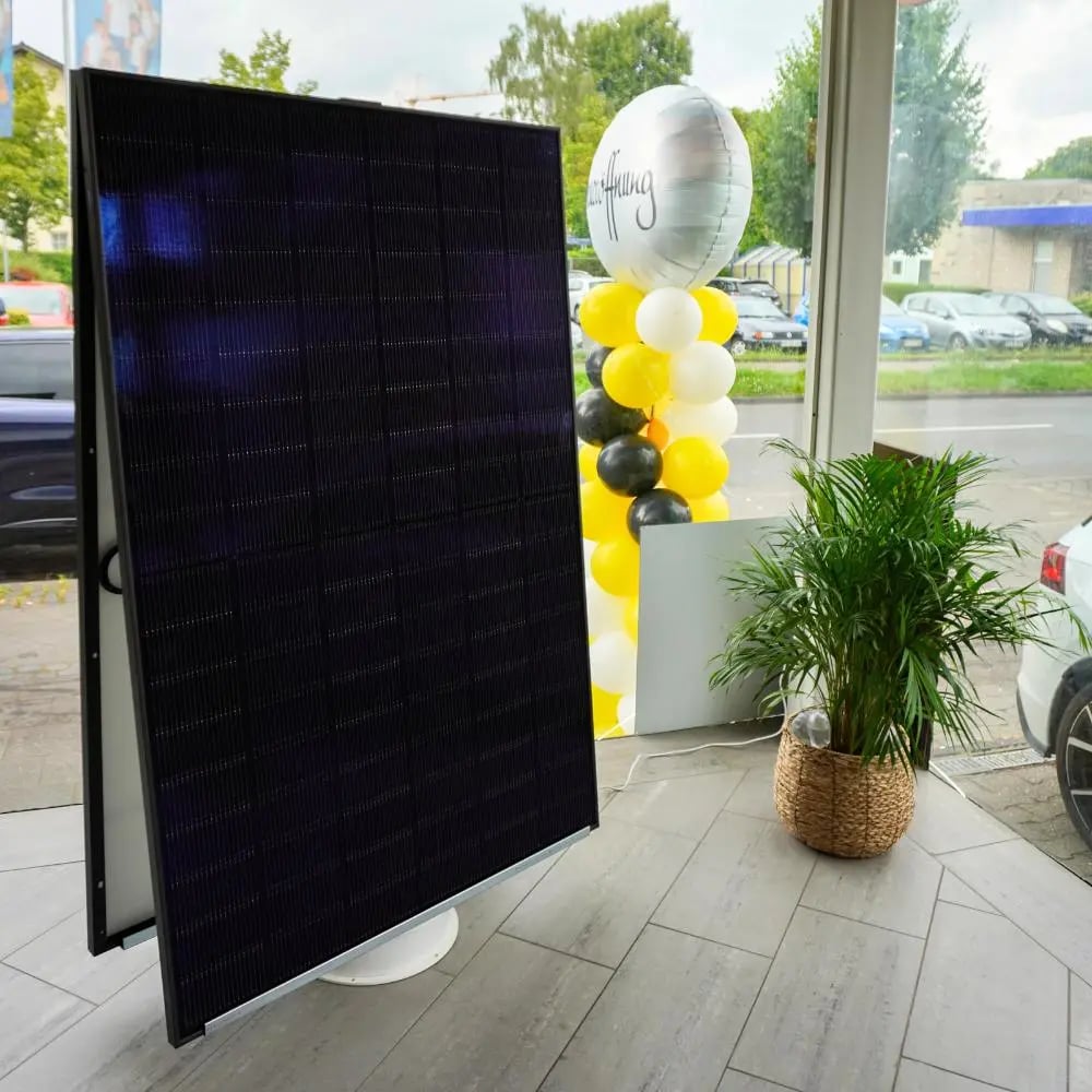 Begrünte Mooswand mit leuchtendem EvoSell-Logo, davor ein aufgeständertes Solarmodul und ein weißer Wandspeicher