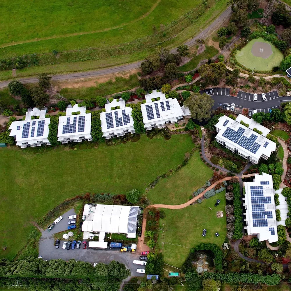 Luftbild einer Wohnanlage im Grünen: mehrere Flachdächer sind mit dunklen Solarmodulen belegt, dazwischen Rasenflächen und Wege