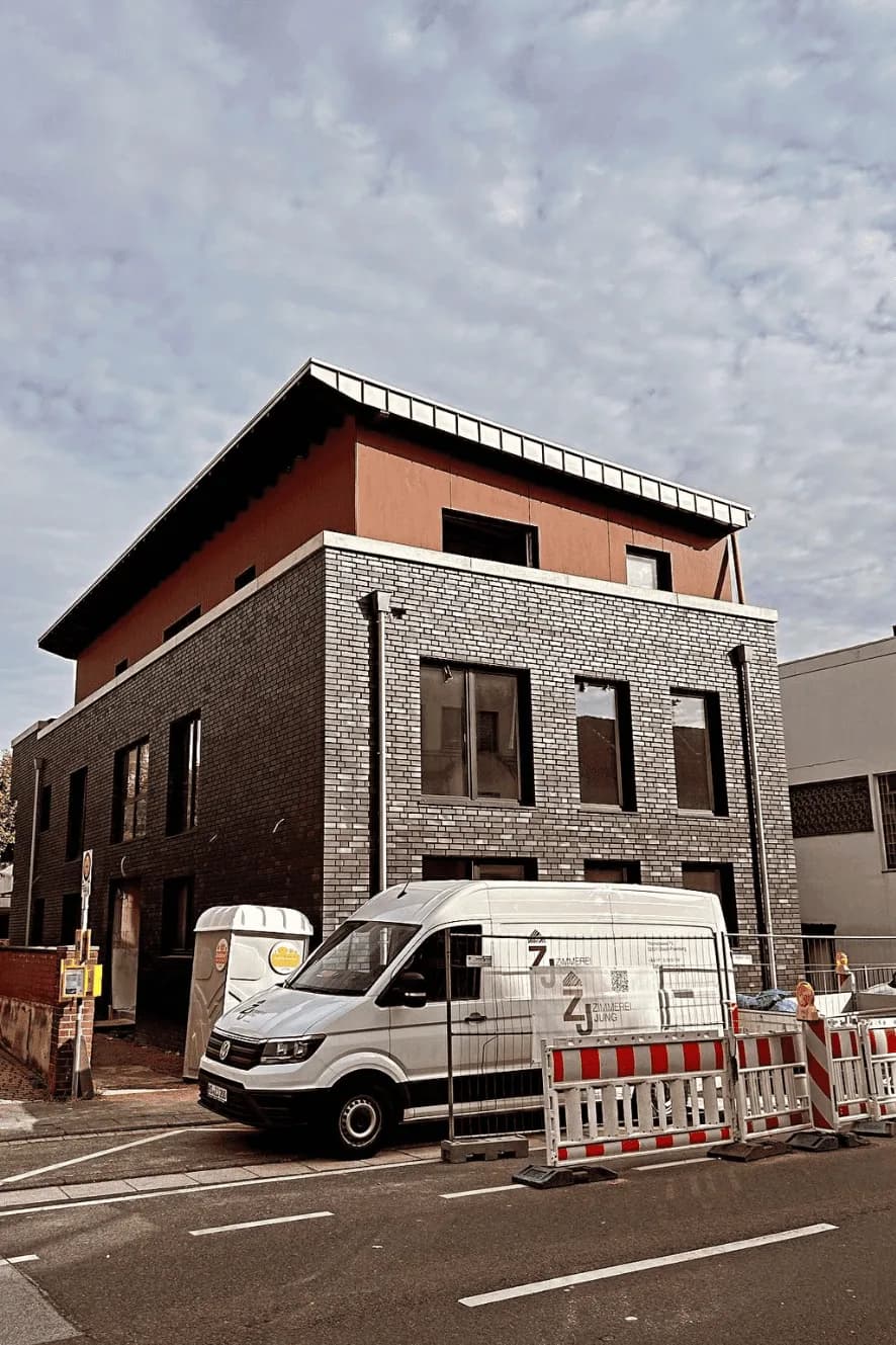 Neubau mit Holzelementen, davor ein Transporter